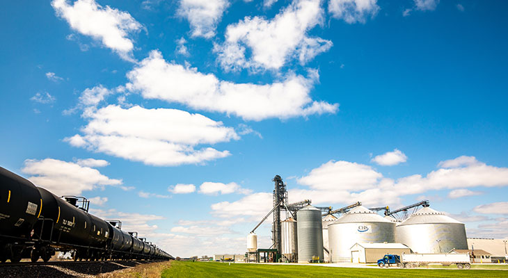 Grain bins beside a railroad track under a cloudy blue sky.